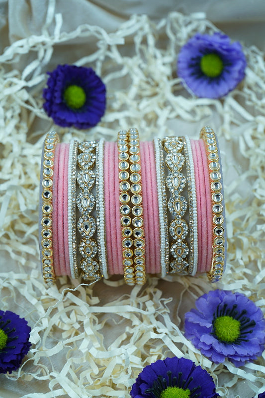 Decorative bangles with pink and gold patterns on a textured surface with purple flowers by hitesh bangles