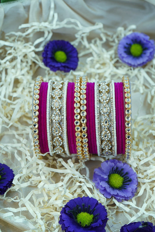 Decorative bangles with purple and gold accents on a white textured background with purple flowers by hitesh bangles