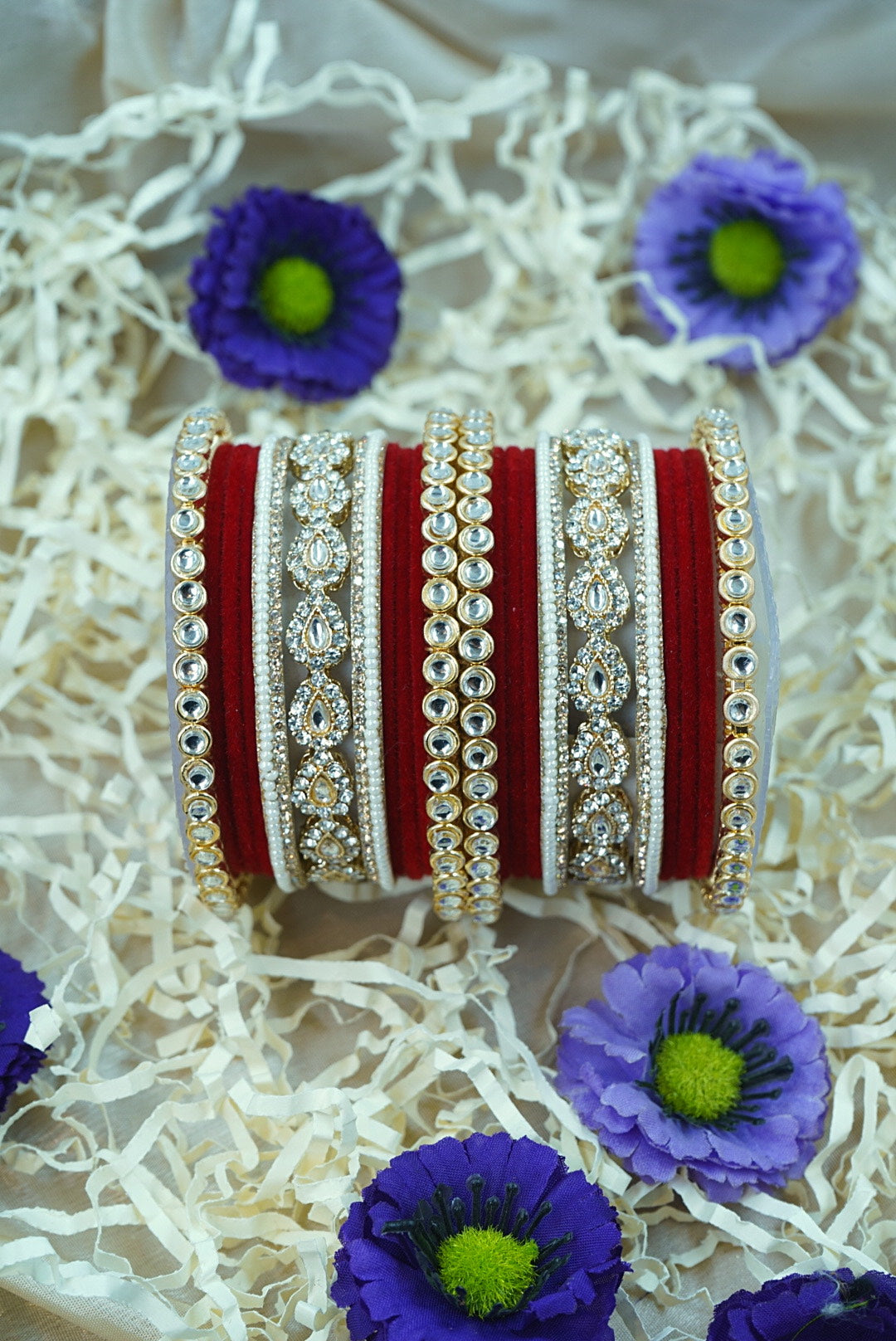 Decorative bangles with intricate designs on a white surface with purple flowers by hitesh bangles