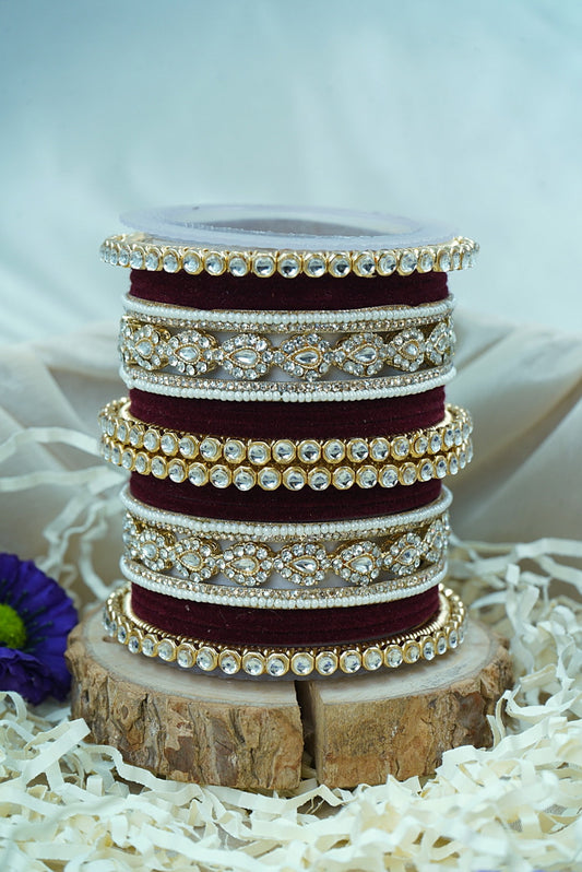 Stack of maroon and gold bangles on a wooden block with a white background by hitesh bangles