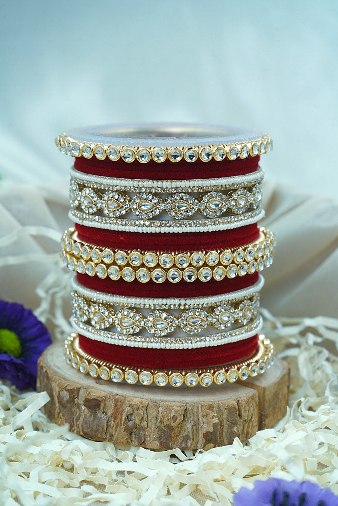 Stack of red and gold bangles on a wooden block with a white background by hitesh bangles