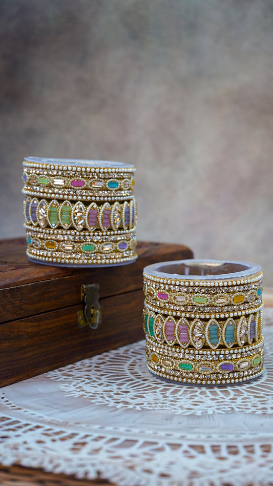 Two ornate bangles with colorful gemstones on a wooden surface by hitesh bangles