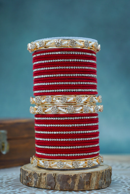 Stack of red bangles with gold and silver accents on a wooden stand against a blue background by hitesh bangles