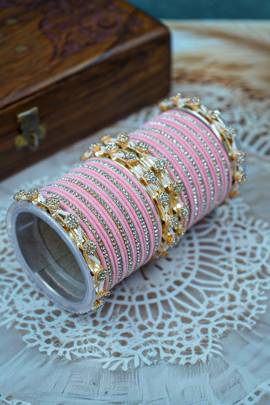 Roll of pink thread with gold and silver embellishments on a textured surface by hitesh bangles