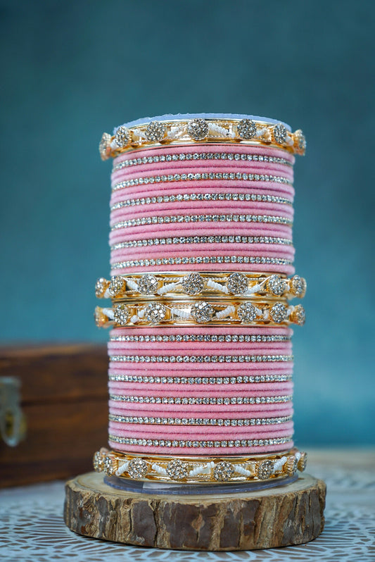 Stack of pink and gold bangles on a wooden stand with a blue background by hitesh bangles
