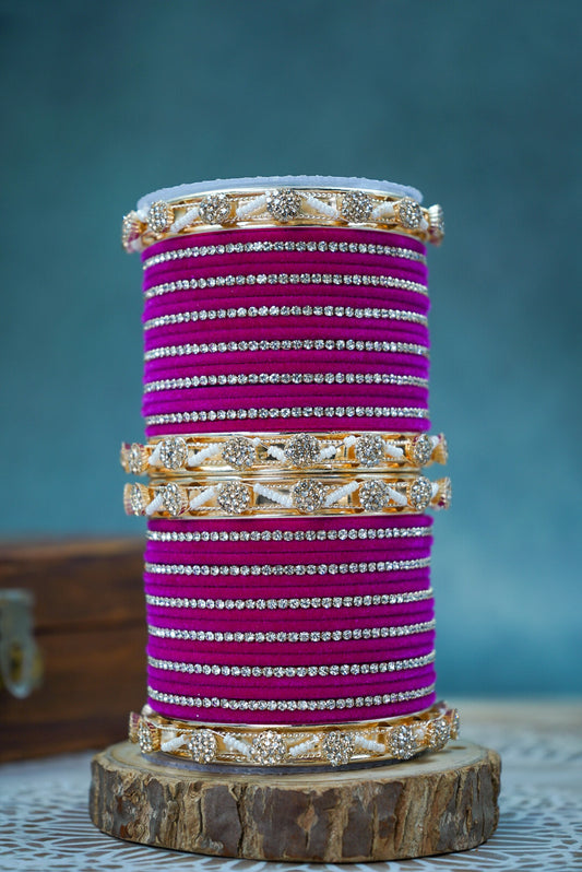 Stack of purple bangles with gold and silver accents on a wooden stand against a blue background by hitesh bangles