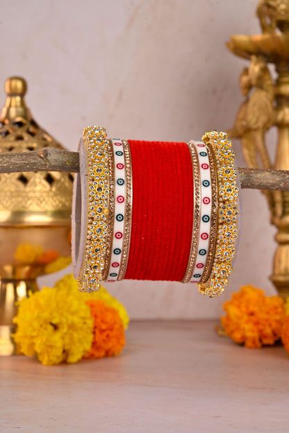 Decorative red bangle with gold and multicolor band on a wooden surface with flowers and decorative items by hitesh bangles