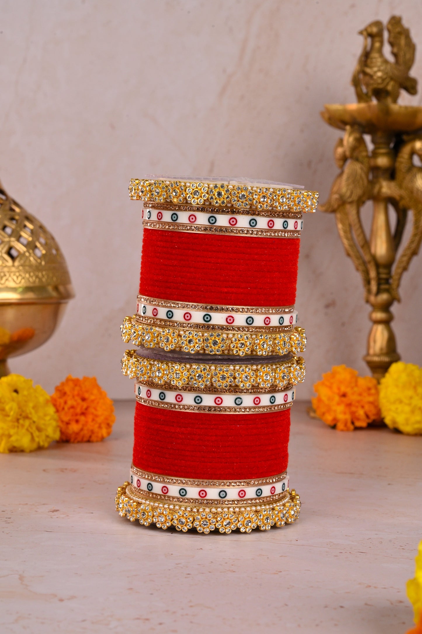 Set of red and gold bangles on a cylindrical stand with decorative elements in the background by hitesh bangles