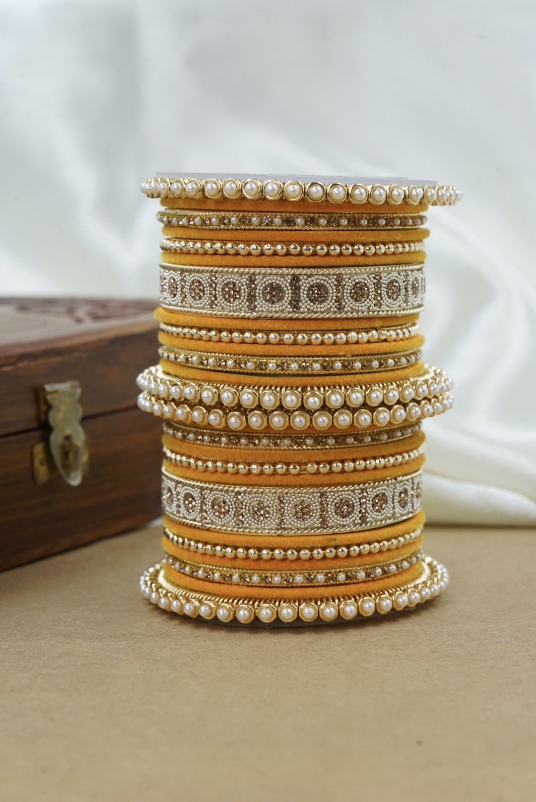 Stack of ornate bangles on a beige surface with a white background by hitesh bangles
