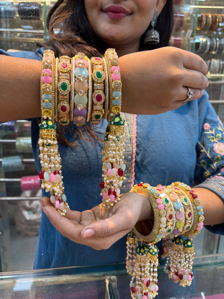 Woman showcasing a set of traditional Indian bridal chooda bangles adorned with multicolored stones, pearls, and gold detailing, featuring dangling beaded tassels.