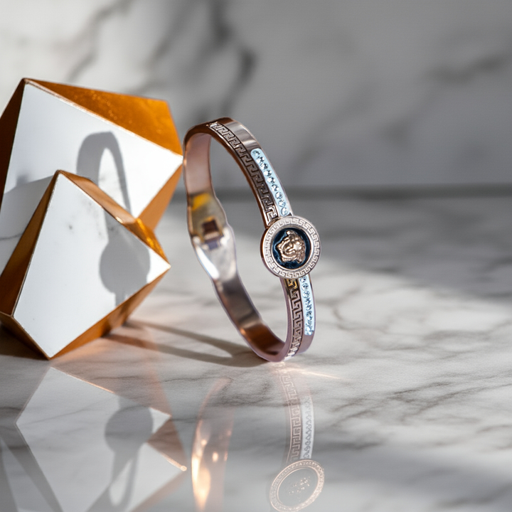 Gold bracelet with a central emblem on a reflective surface by hitesh bangles