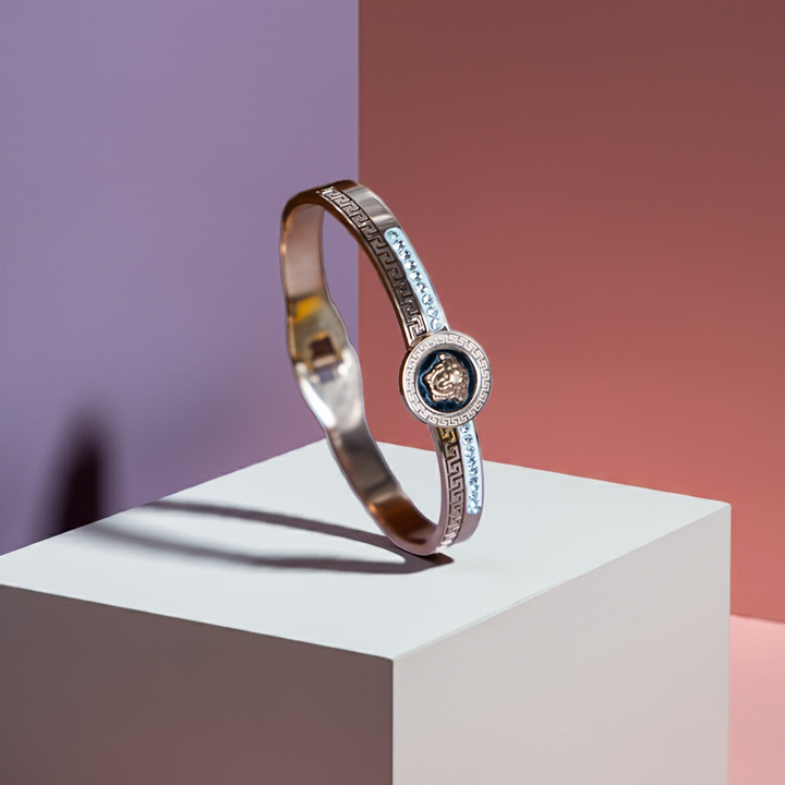 Gold bracelet with a central emblem on a white platform against a gradient background by hitesh bangles