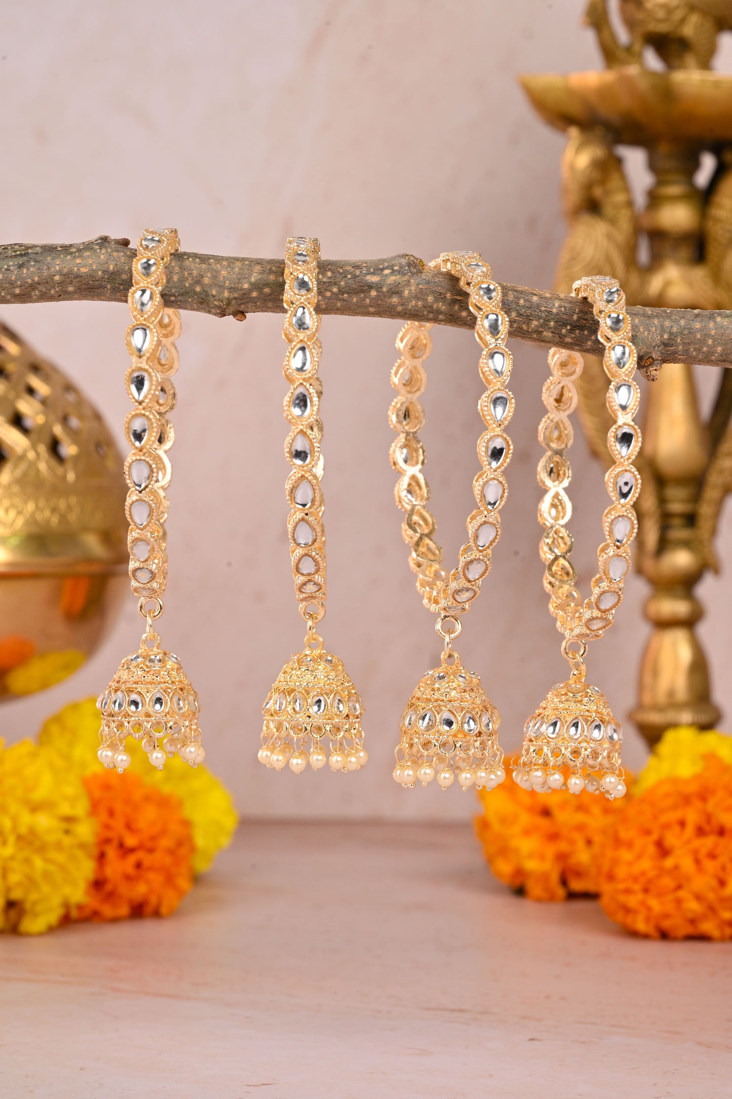 Gold earrings with jhumki design on a branch with flowers and decorative items in the background by hitesh bangles