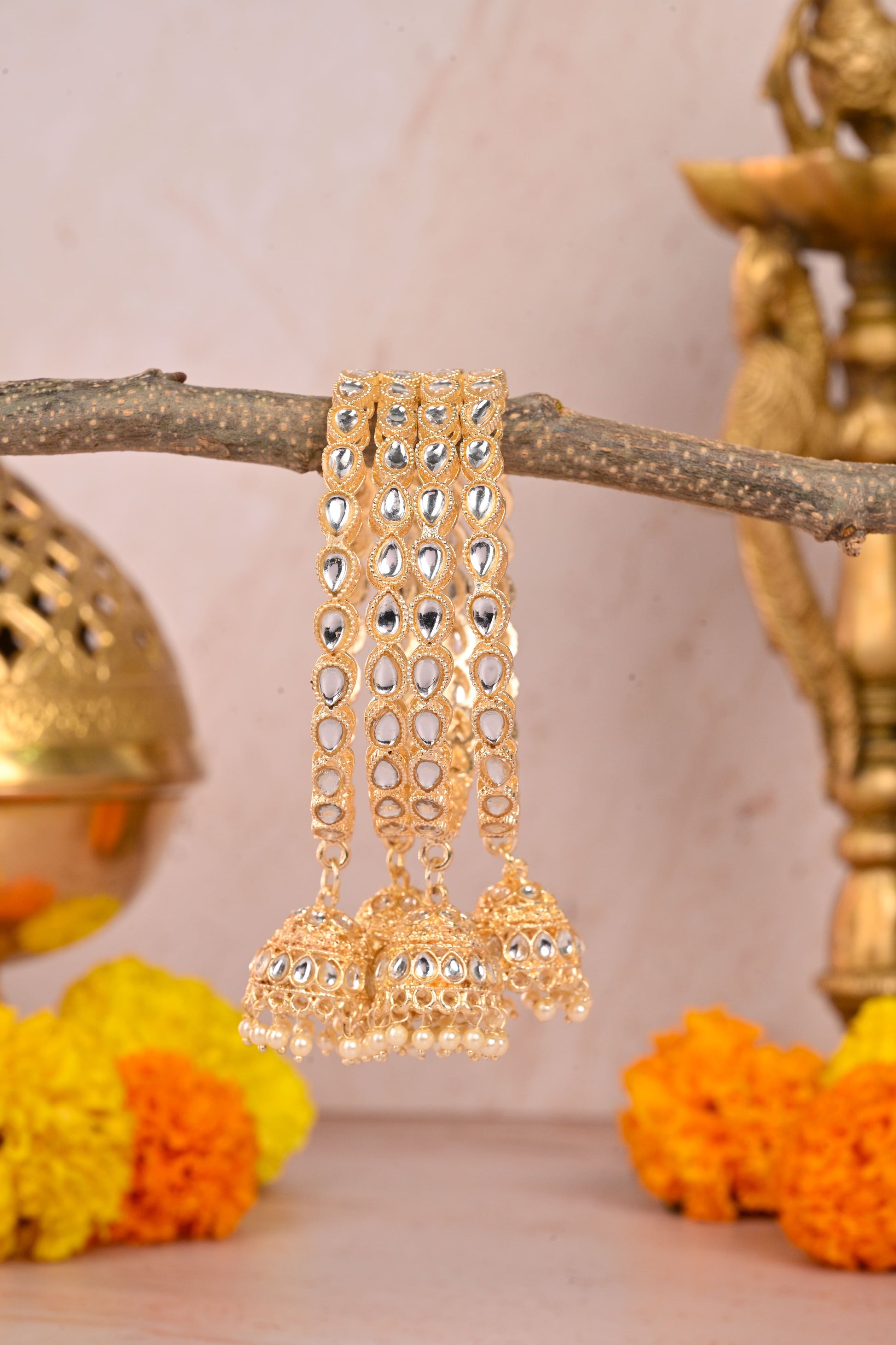 Gold earrings with intricate designs on a branch with marigold flowers and a decorative object in the background by hitesh bangles