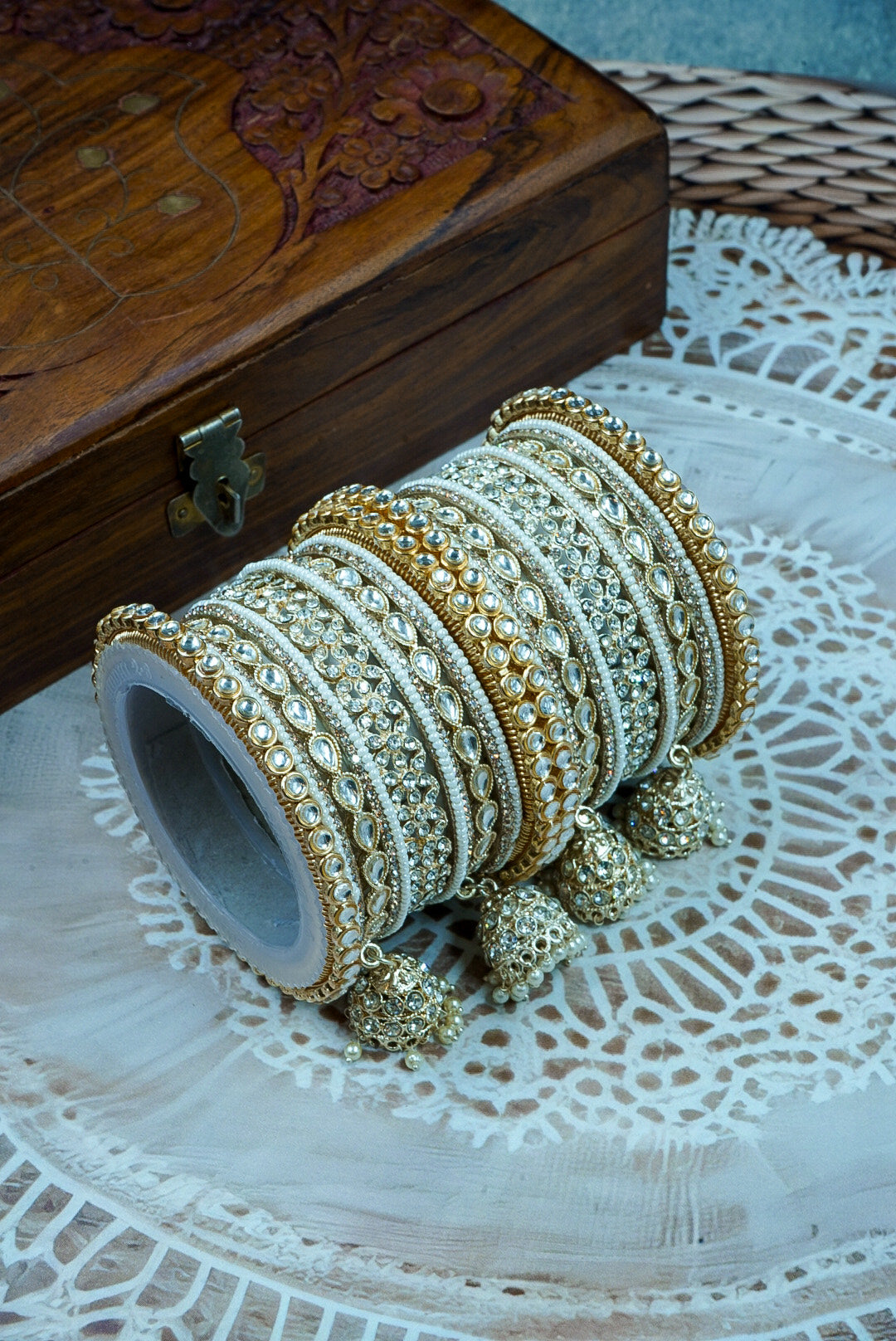 Set of gold and white bangles on a wooden box with a lace tablecloth background by hitesh bangles