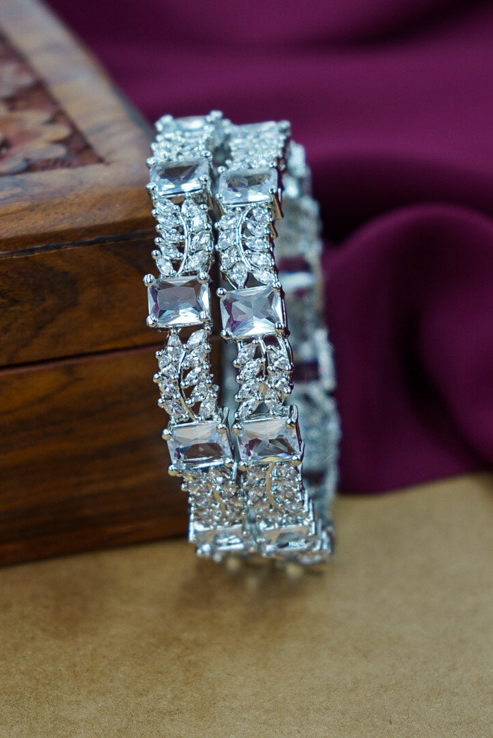 Silver bracelet with square-cut gemstones on a wooden surface with a purple fabric background by hitesh bangles