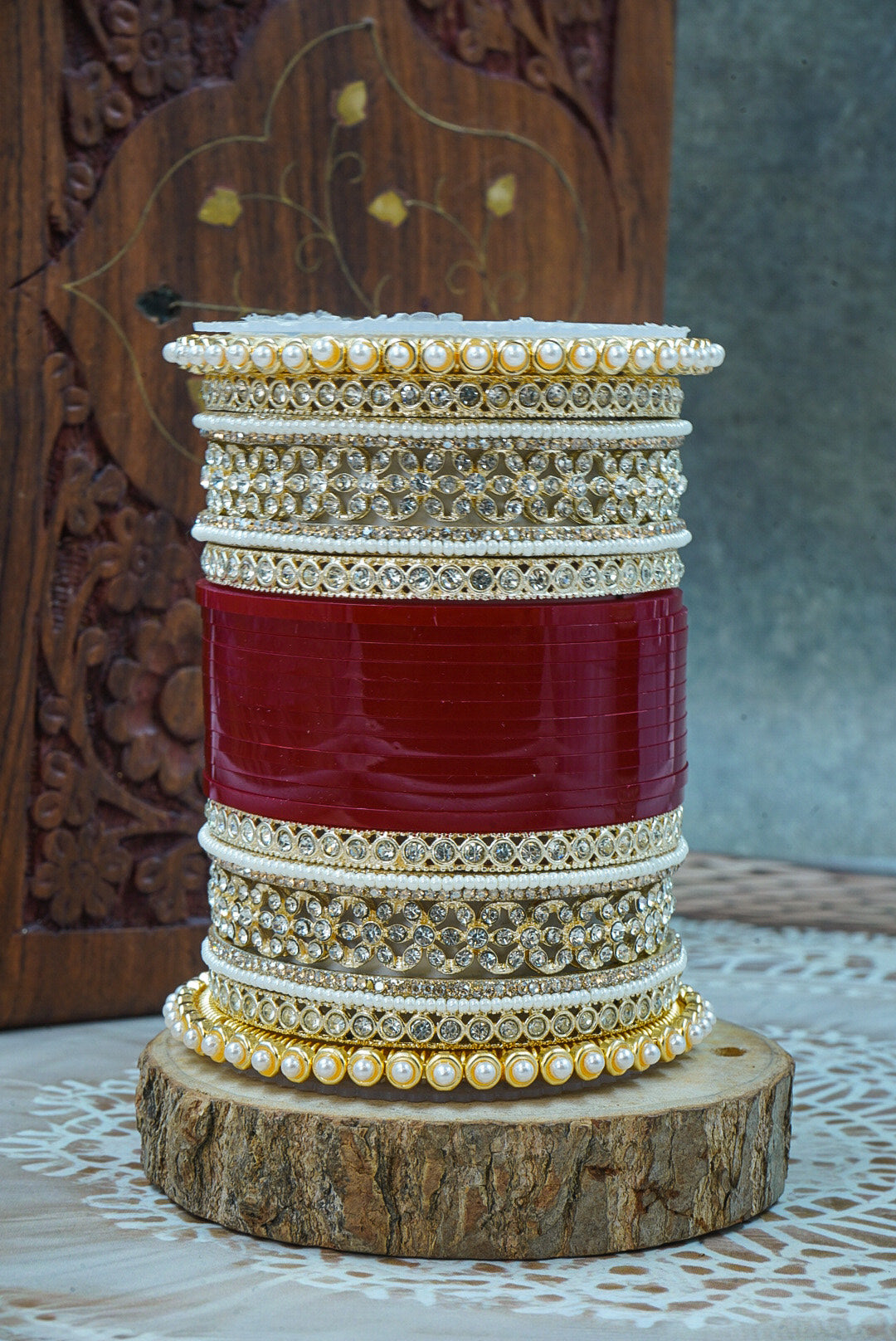 Stack of gold and white bangles on a red background, displayed on a wooden stand with a decorative background by hitesh bangles