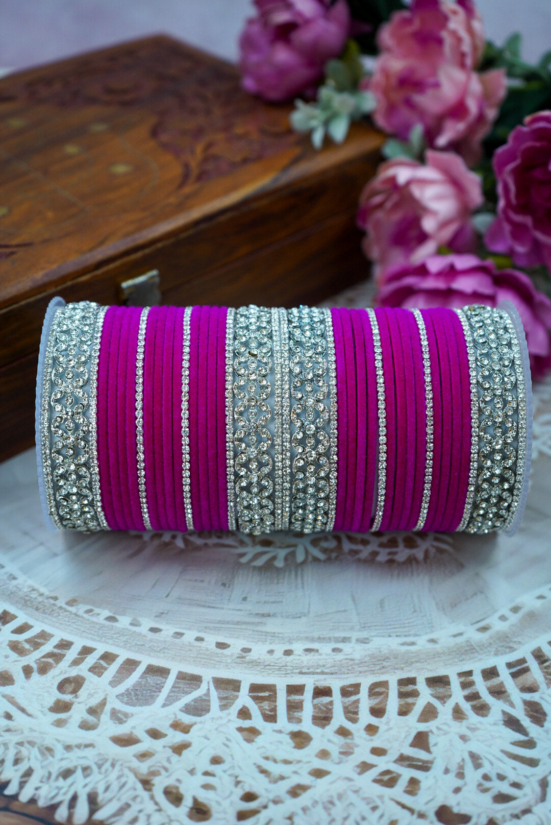 Decorative bangle roll with pink and silver stripes on a lace surface with flowers in the background by hitesh bangles