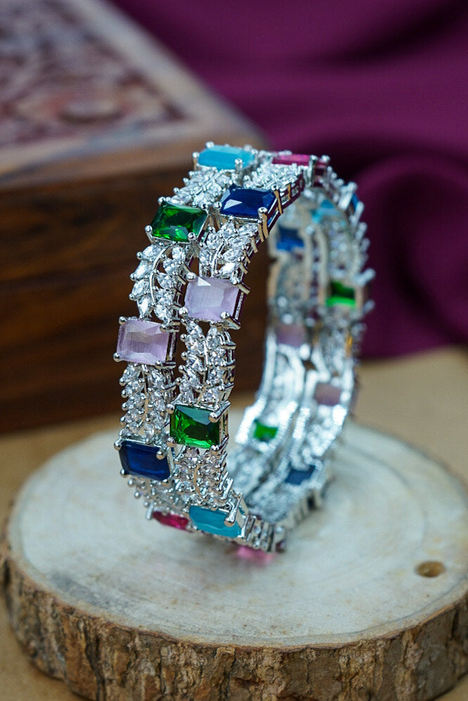 Pair of silver hoop earrings with colorful gemstones on a wooden surface by hitesh bangles