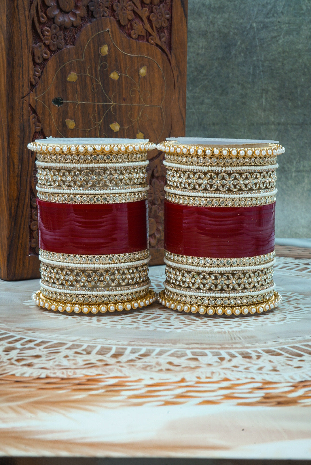 Two red and gold bangles on a wooden surface with a textured background by hitesh bangles
