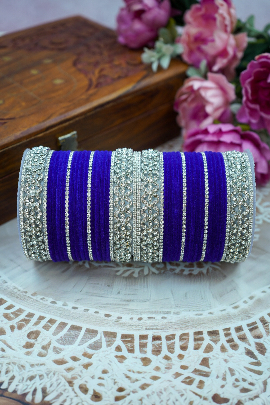 Decorative purple and silver bangle on a lace surface with flowers in the background by hitesh bangles