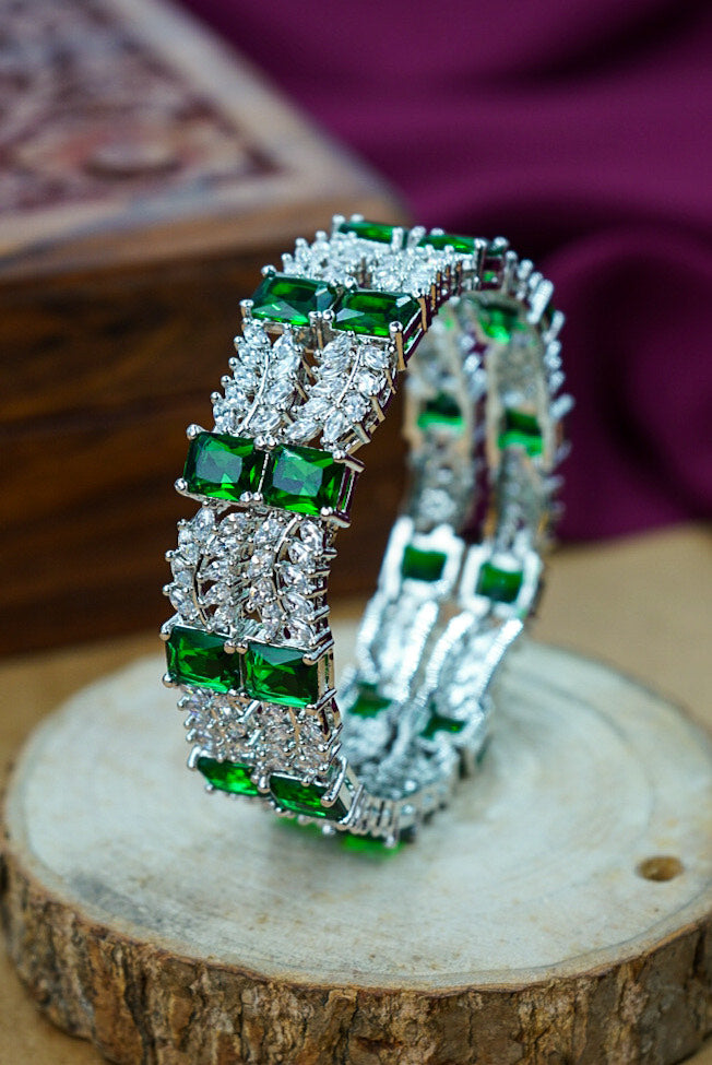 Pair of emerald and diamond earrings on a wooden surface with a blurred background by hitesh bangles