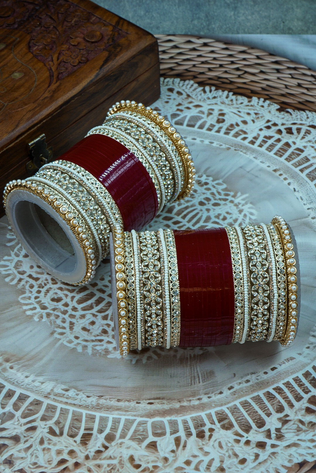 Pair of red and gold bangles on a textured surface by hitesh bangles