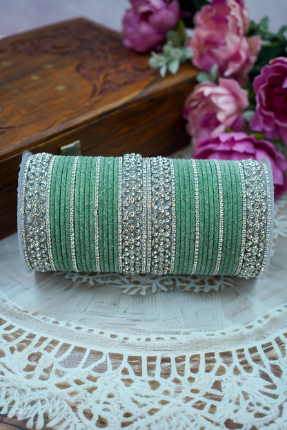 Green and silver bracelet roll on a lace surface with flowers in the background by hitesh bangles