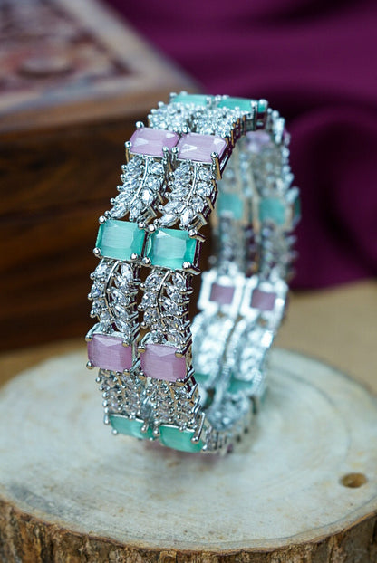 Pair of silver hoop earrings with green and pink gemstones on a wooden surface by hitesh bangles