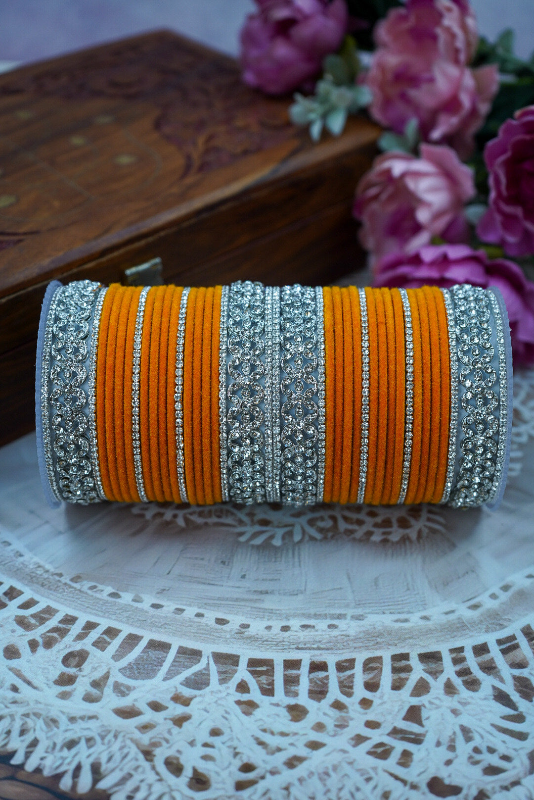Decorative clutch with orange and silver stripes on a lace tablecloth with flowers in the background by hitesh bangles