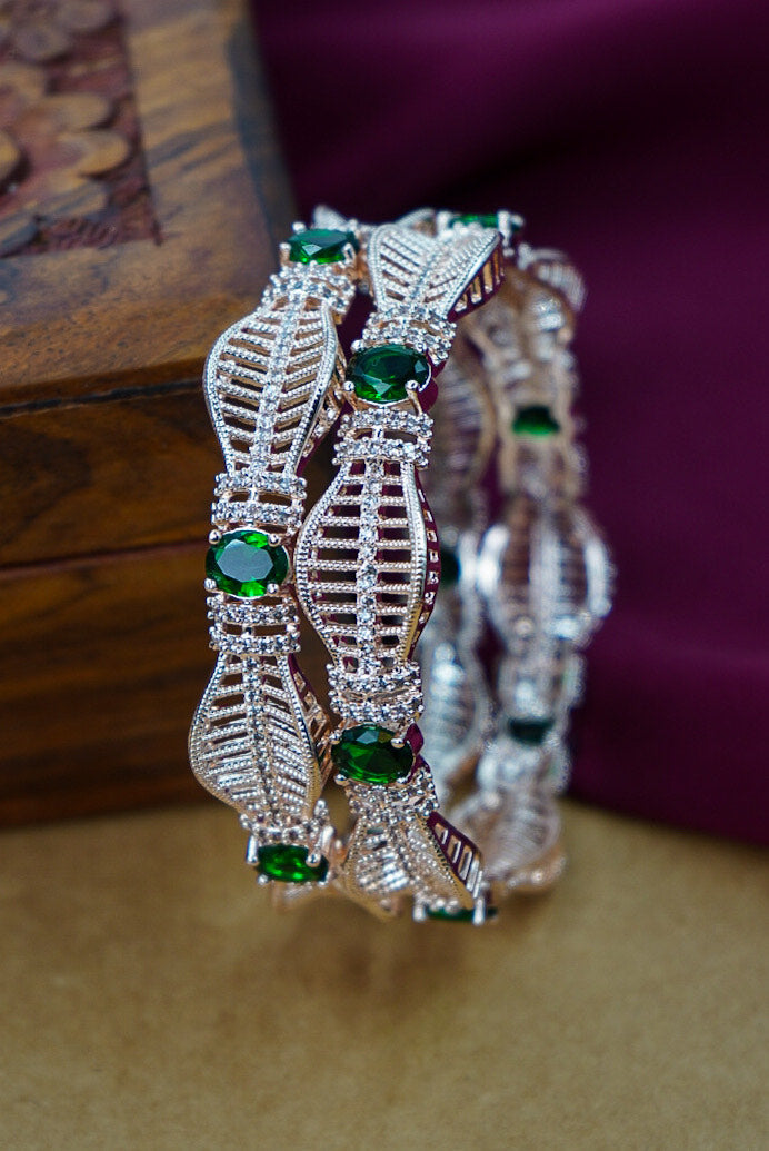 Decorative silver bangles with green gemstones on a wooden surface by hitesh bangles