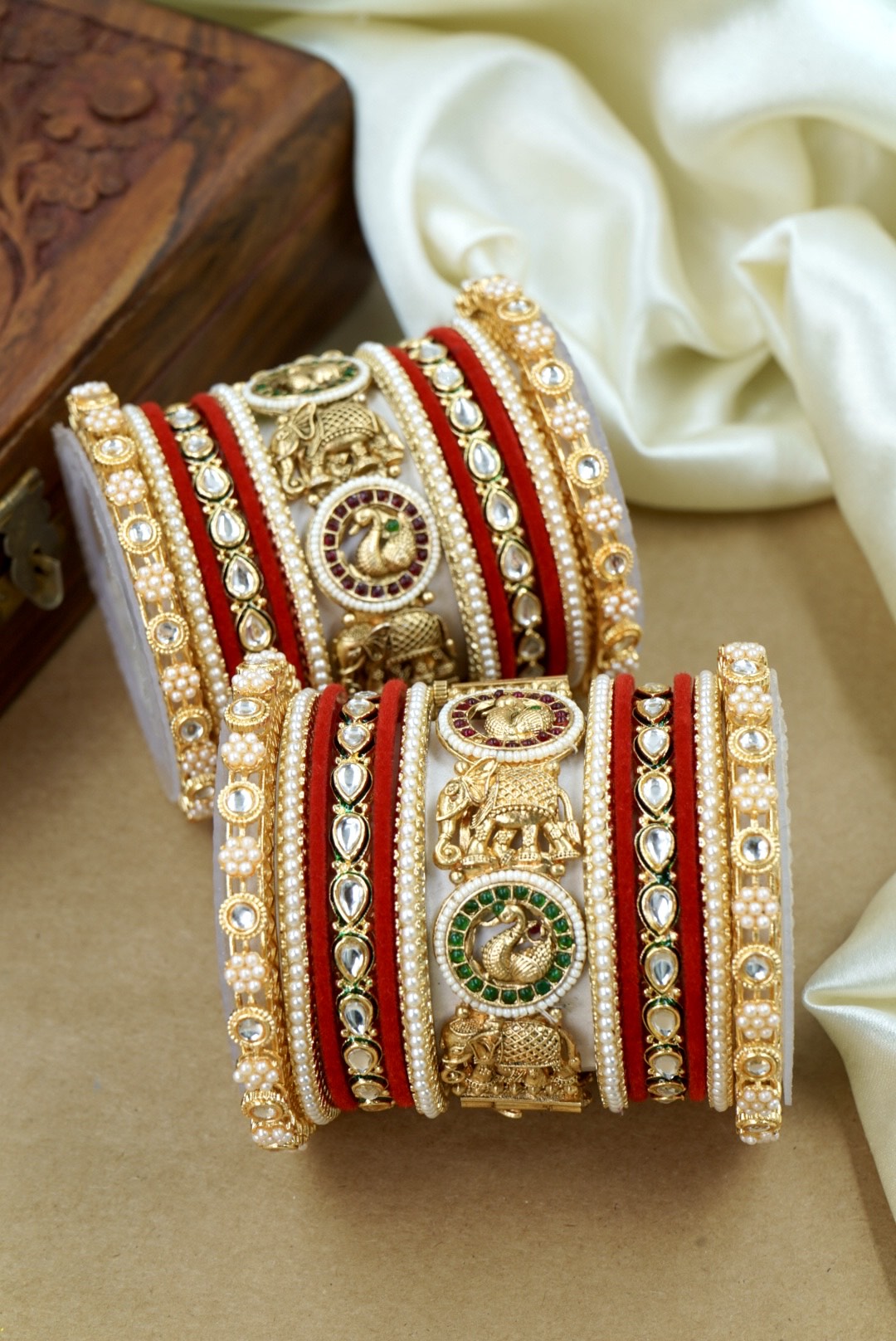 Decorative bangles with gold and red bands on a white fabric background by hitesh bangles