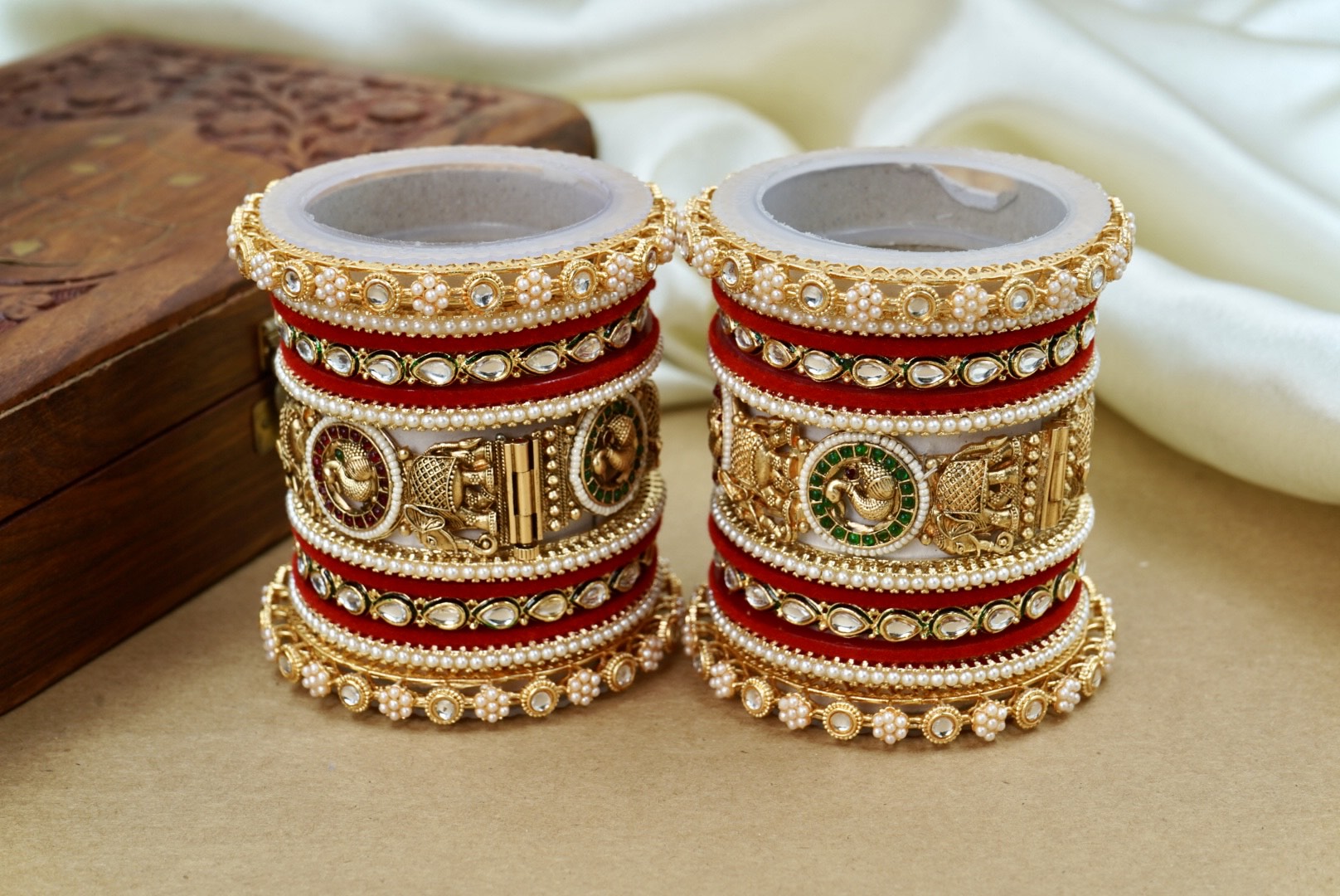 Pair of ornate bangles with gold and red design on a beige surface by hitesh bangles