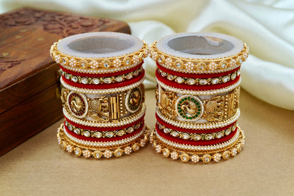 Pair of ornate bangles with gold and red design on a beige surface by hitesh bangles