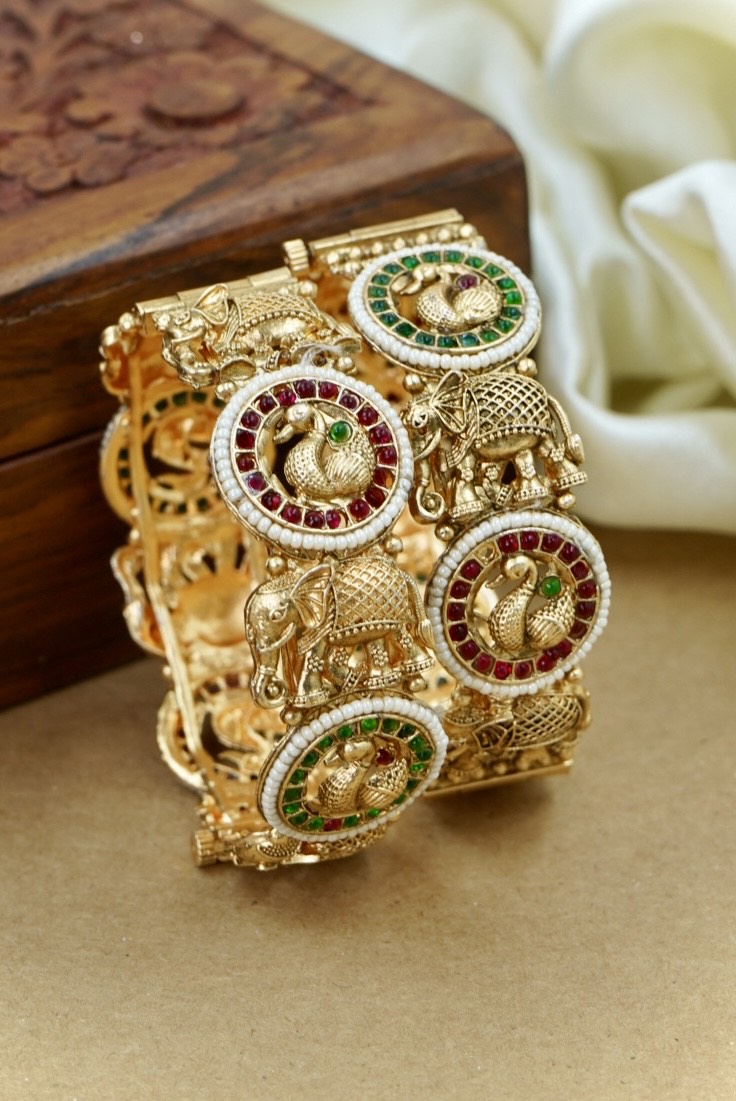 Gold bracelet with elephant and gemstone designs on a wooden surface by hitesh bangles