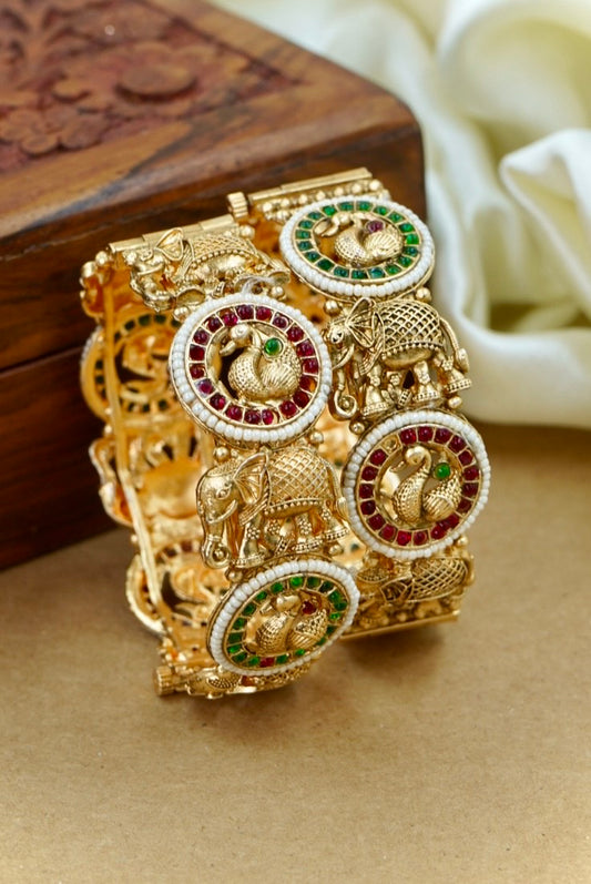 Gold bracelet with elephant and gemstone designs on a wooden surface by hitesh bangles
