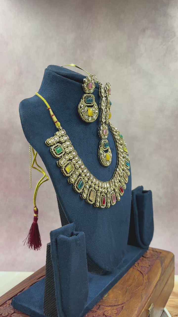 Traditional Kundan necklace set with multicolor stones and matching earrings displayed on a blue velvet stand – elegant Indian bridal jewelry design by hitesh bangles